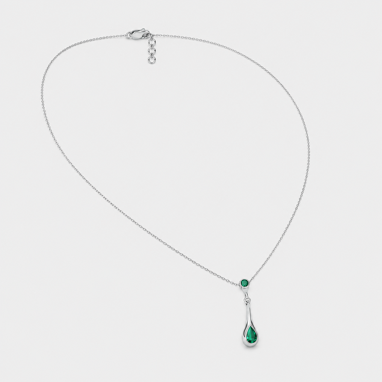 Angled view of silver-tone necklace with emerald green teardrop cubic zirconia pendant and adjustable extension chain