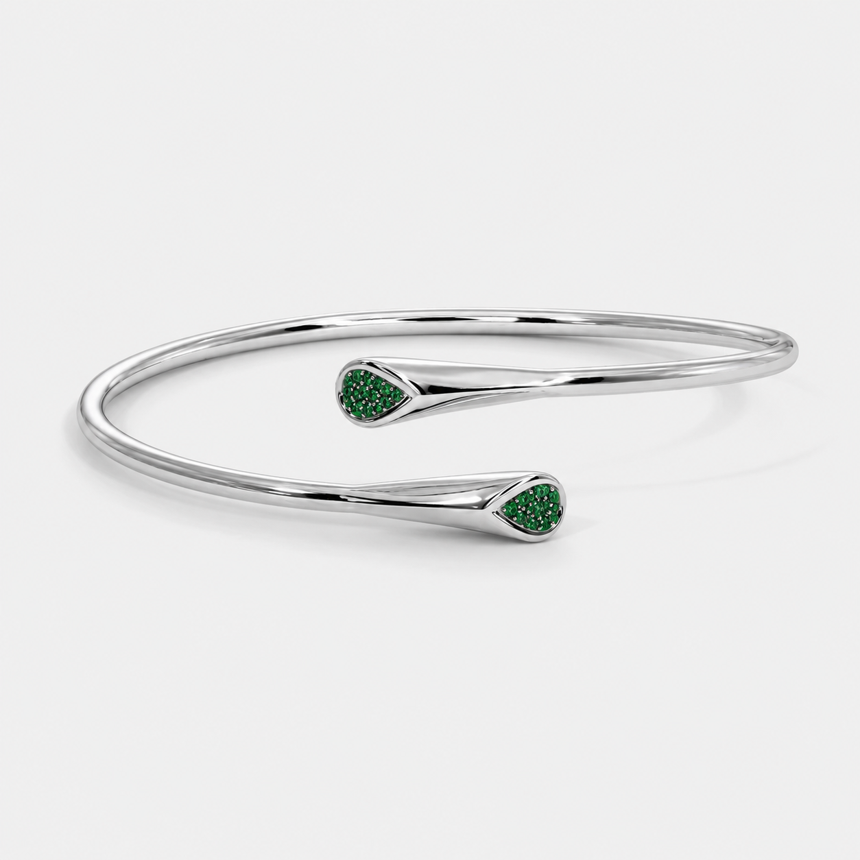 Angled view of silver-tone cuff bracelet with emerald green stone accents and polished