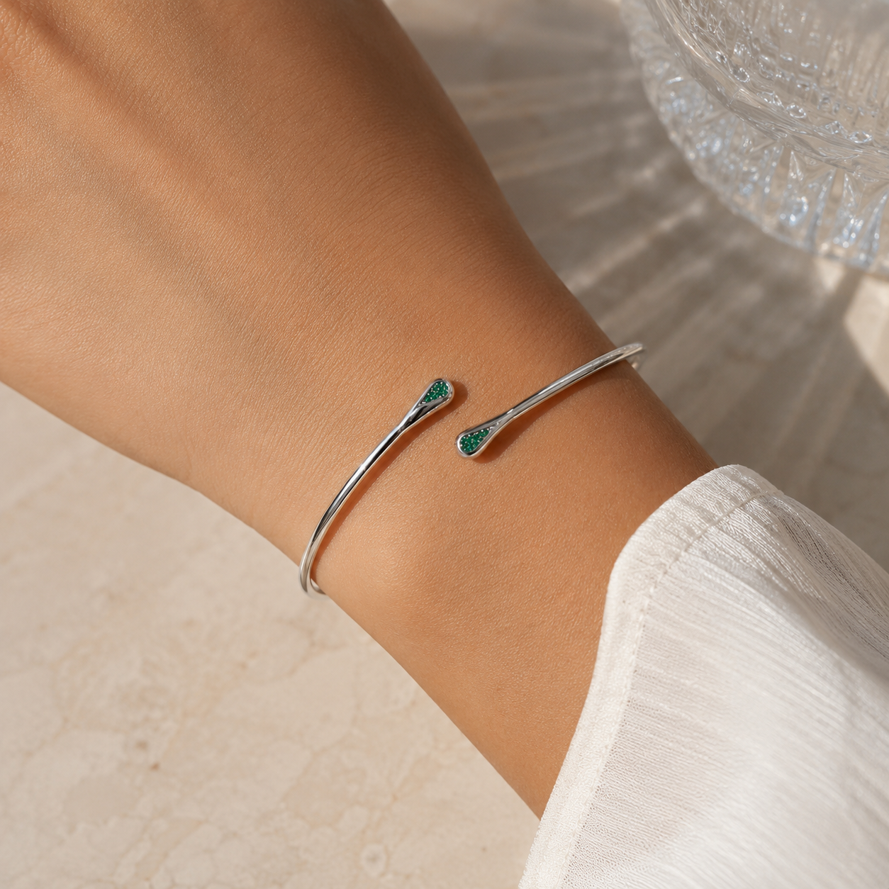 Woman wearing a silver-tone open cuff bracelet with emerald green cubic zirconia accents on the wrist