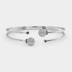 Angled view of silver-tone bracelet with dual band design, openwork spheres, and emerald green stone accents