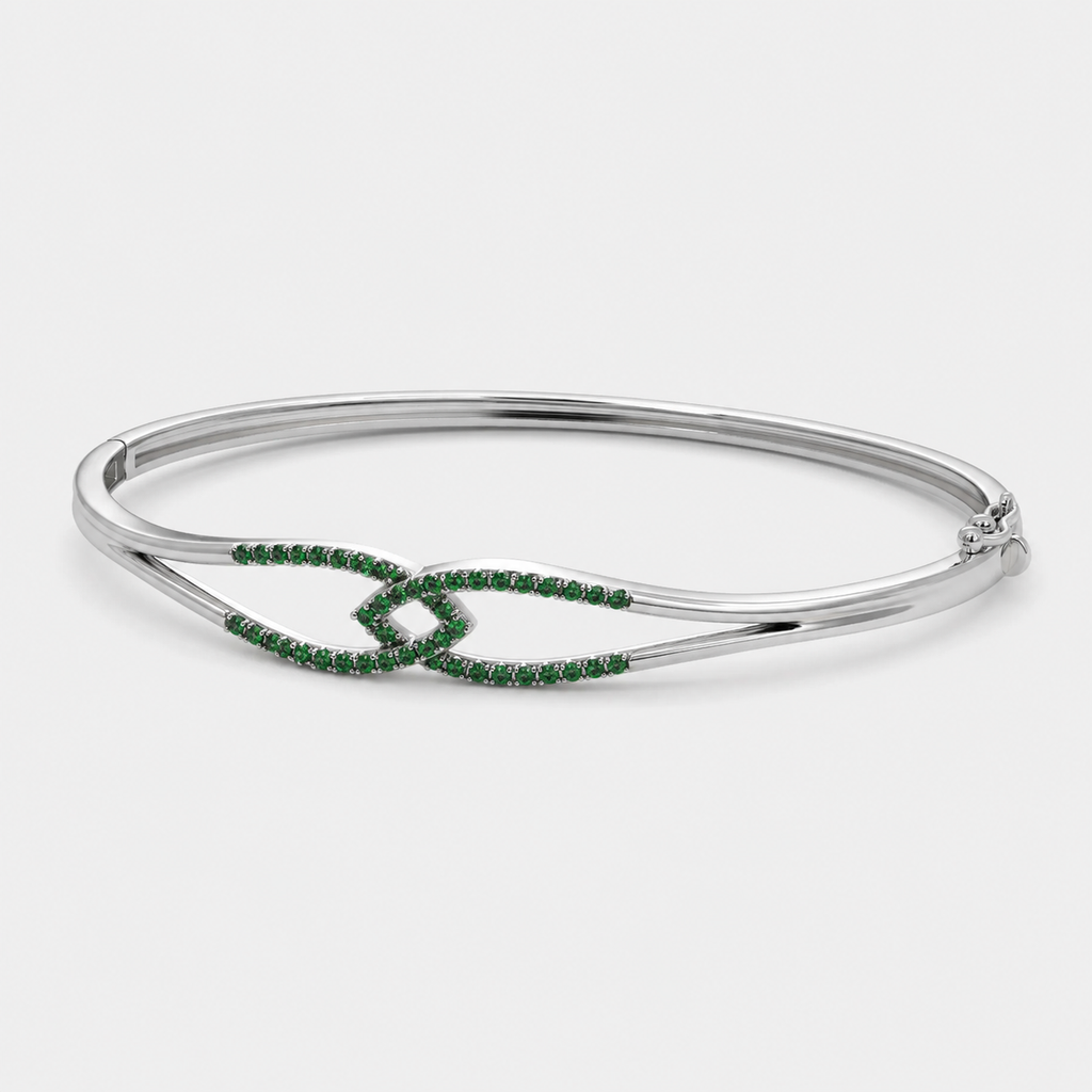 Angled view of silver-tone cuff bracelet with emerald green stone accents and polished finish