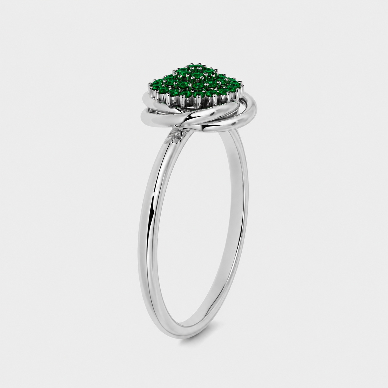 Angled view of silver-tone floral-inspired cluster ring with emerald green stone accents and polished finish