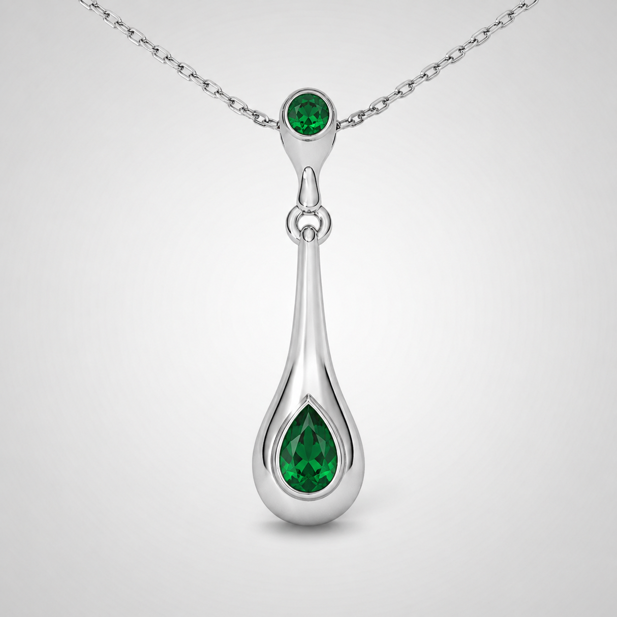 Close-up view of emerald green teardrop pendant suspended from a fine silver-tone chain