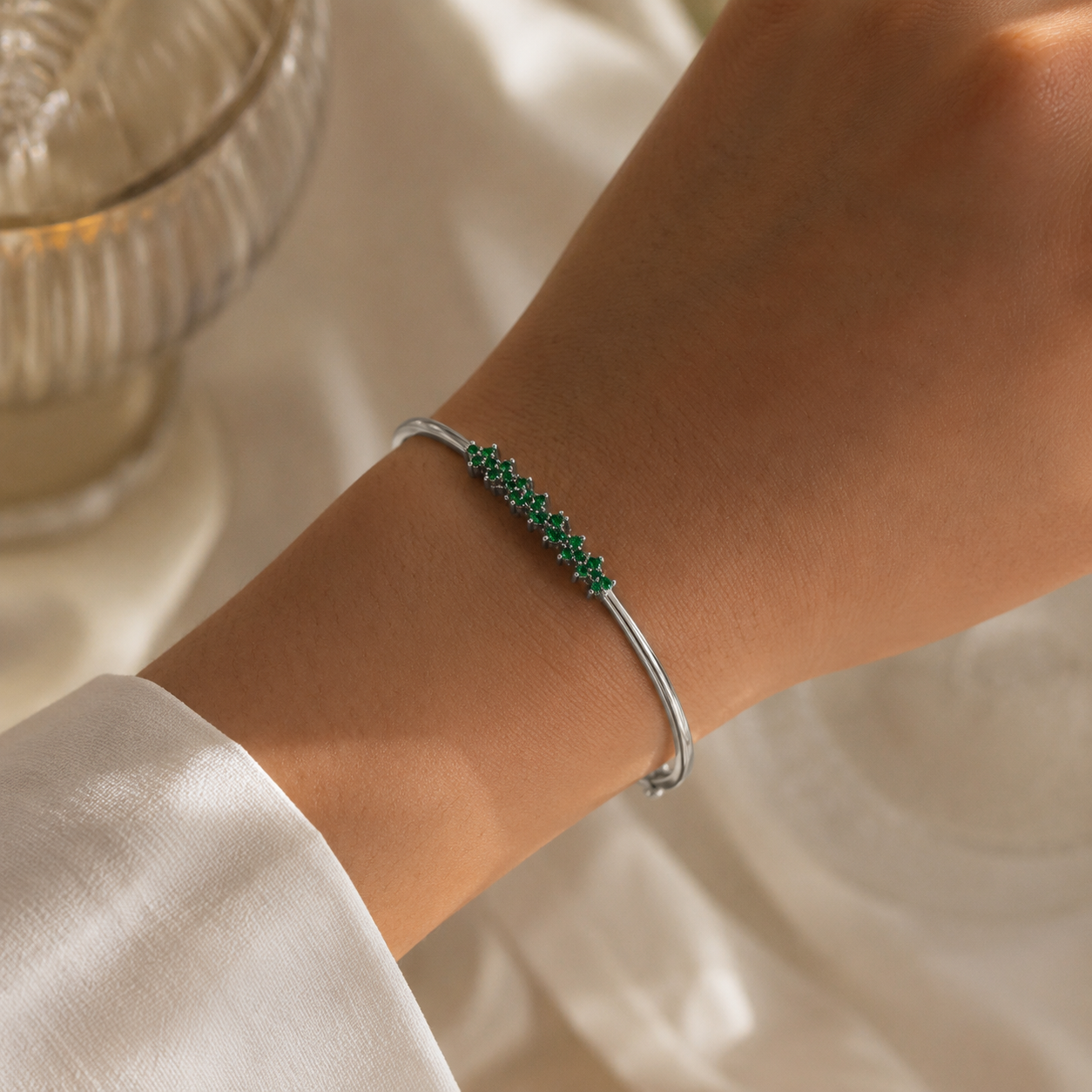 Woman wearing a silver-tone bangle bracelet with emerald green cubic zirconia accents on the wrist
