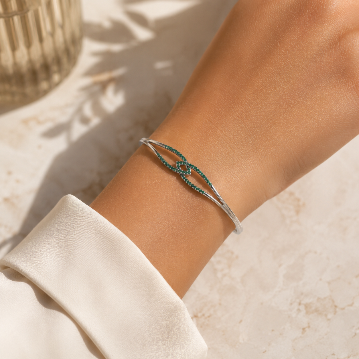 Woman wearing a silver-tone open cuff bracelet with emerald green cubic zirconia accents on the wrist